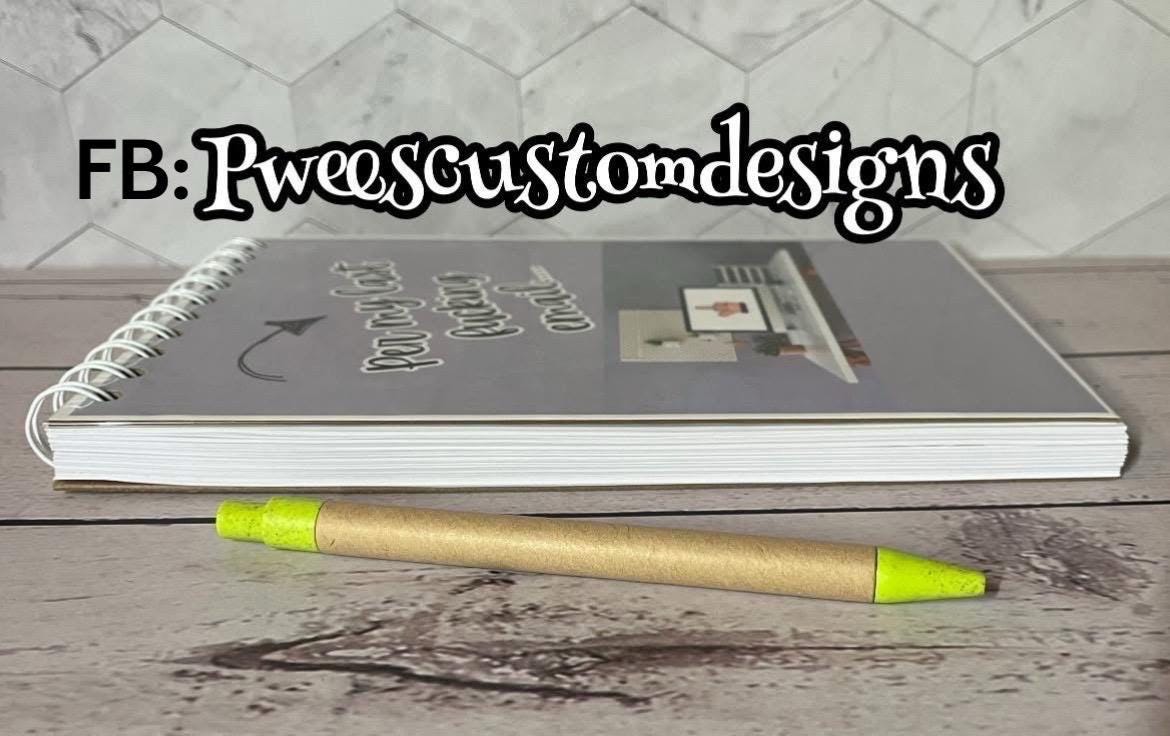 Notebook with a pen on a wooden surface, featuring text 'FB: Pweescustomdesigns'.